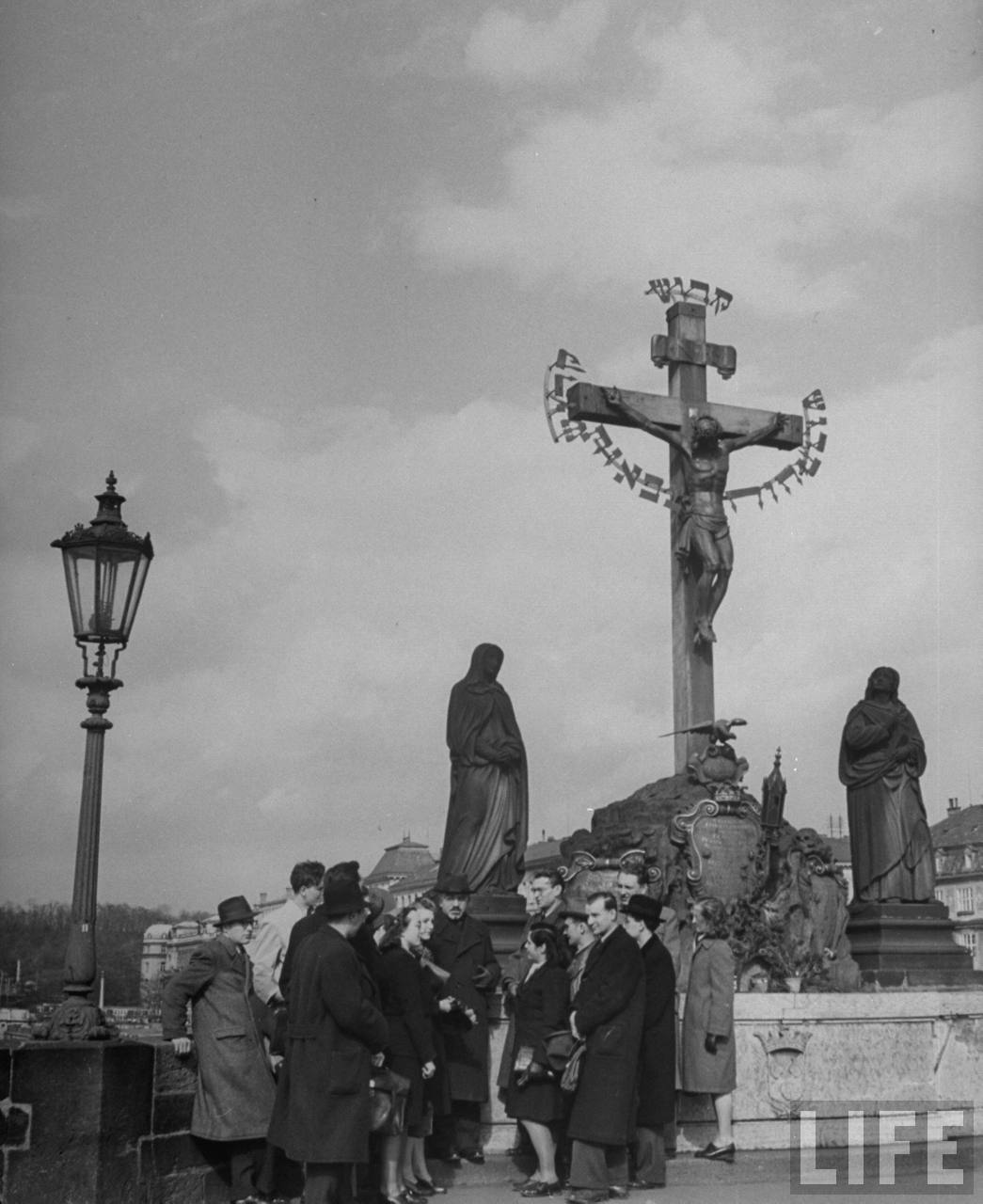 Charles University history class studying crucifix on historic Charles Bridge.