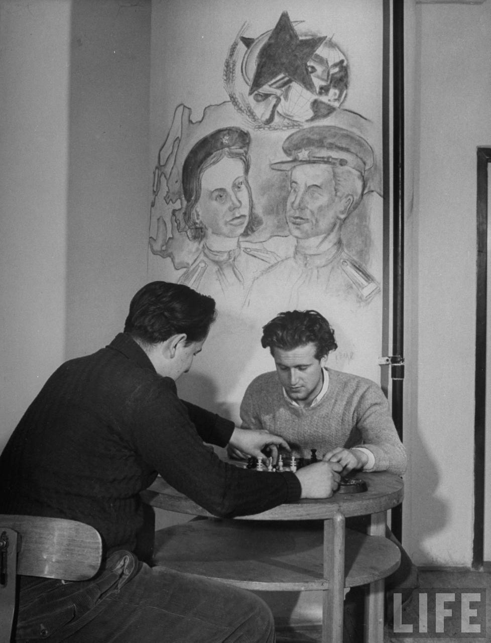 Two Czech students playing chess under student artwork on wall of room in the Marshal Tito Hall at Charles University.